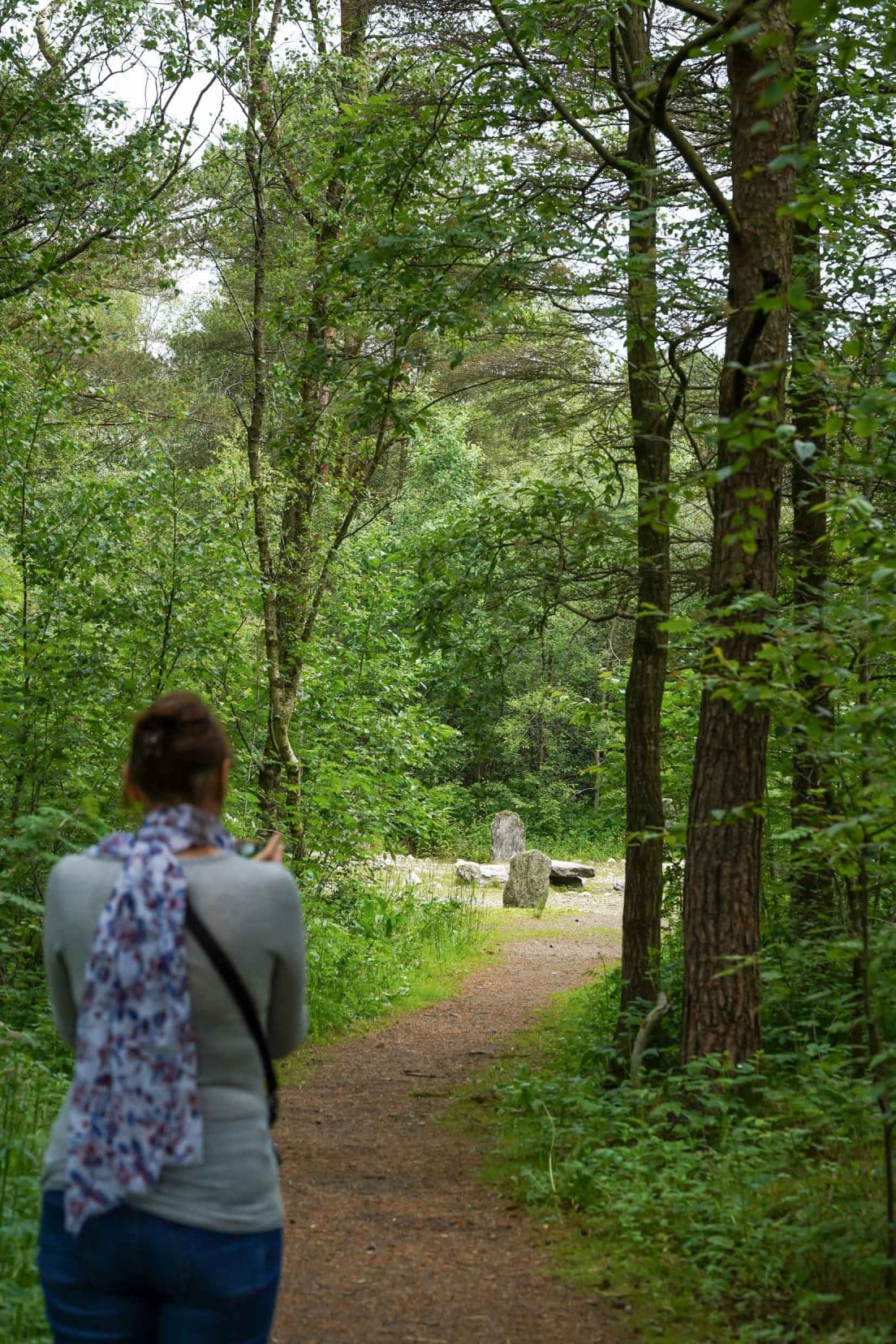 Shelley walking along a small sandy path lined by trees to the opening of the granite stones in a circle 
