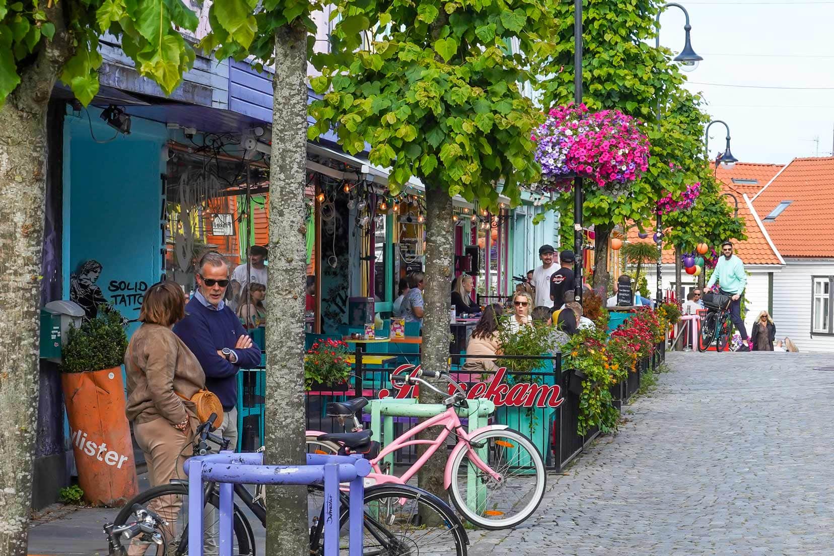 colourful street in Stavanger with lots of hanging baskets and floral displays and outdoor tables by cafes 