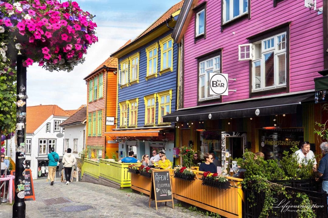 Colourful wooden houses with cafes on teh first floor, outside seating and lots of flowers decorating the street