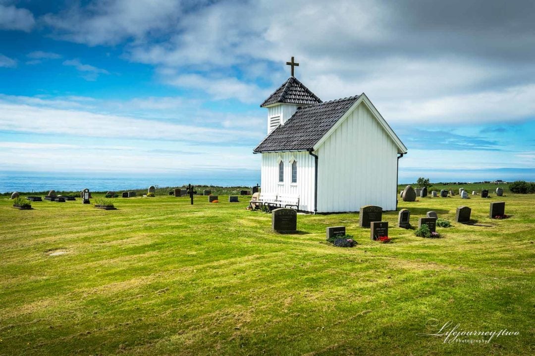 small white chapel on green filed with a few gravestones and sea in the background