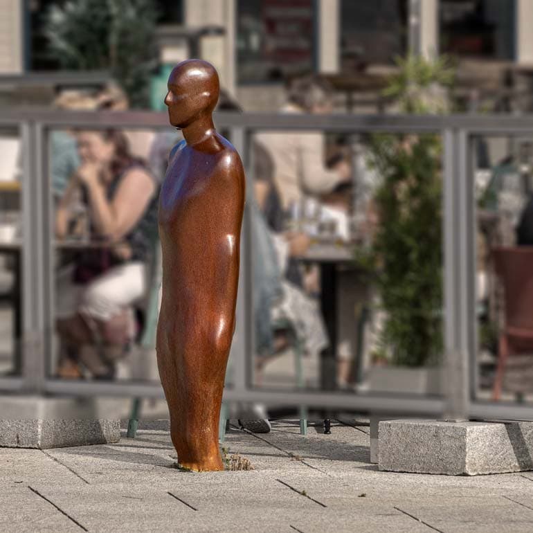 rust coloured statue of a man with only above the news ppping out of the ground