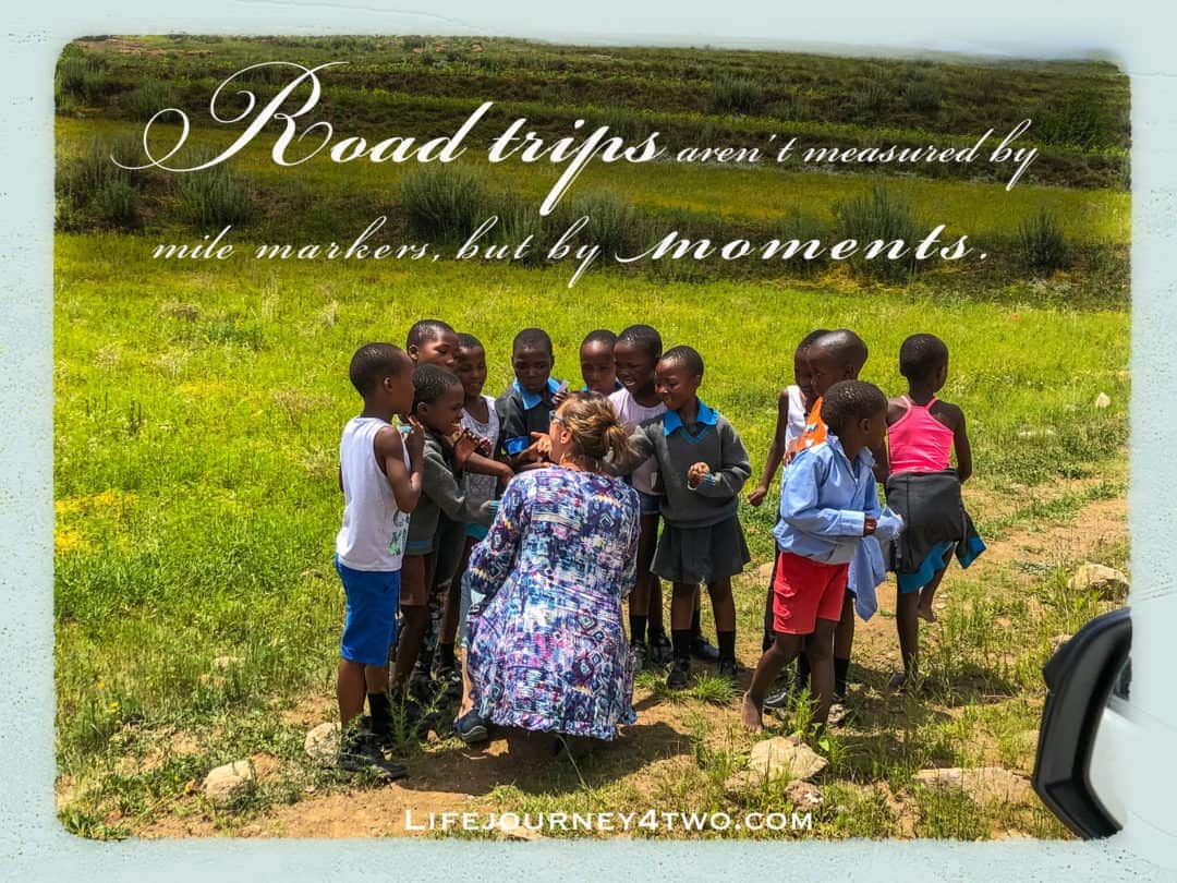 Road trip quote on an image f woman surrounded by small children in Africa on teh side of a road