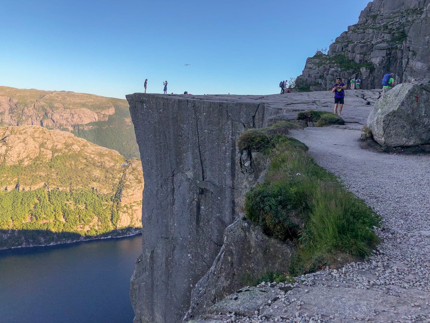 Flat rock plateau with people stnading on top with a fjord below