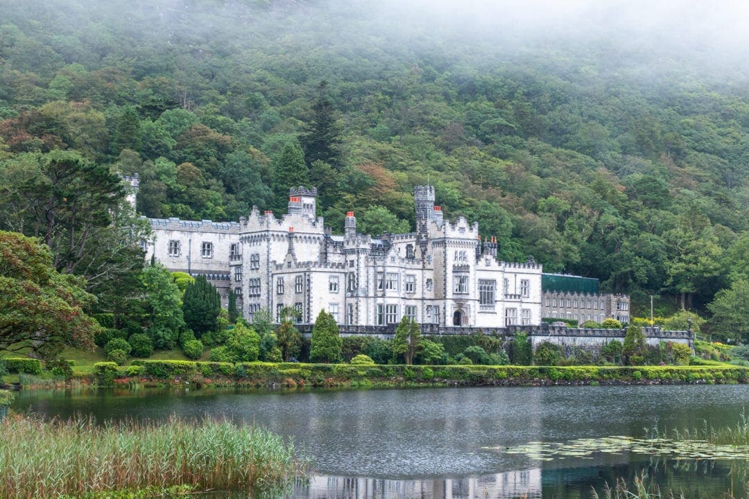 Ireland Landscape Photography: White stoned abbey with a lake in front and a green steep mountain behind