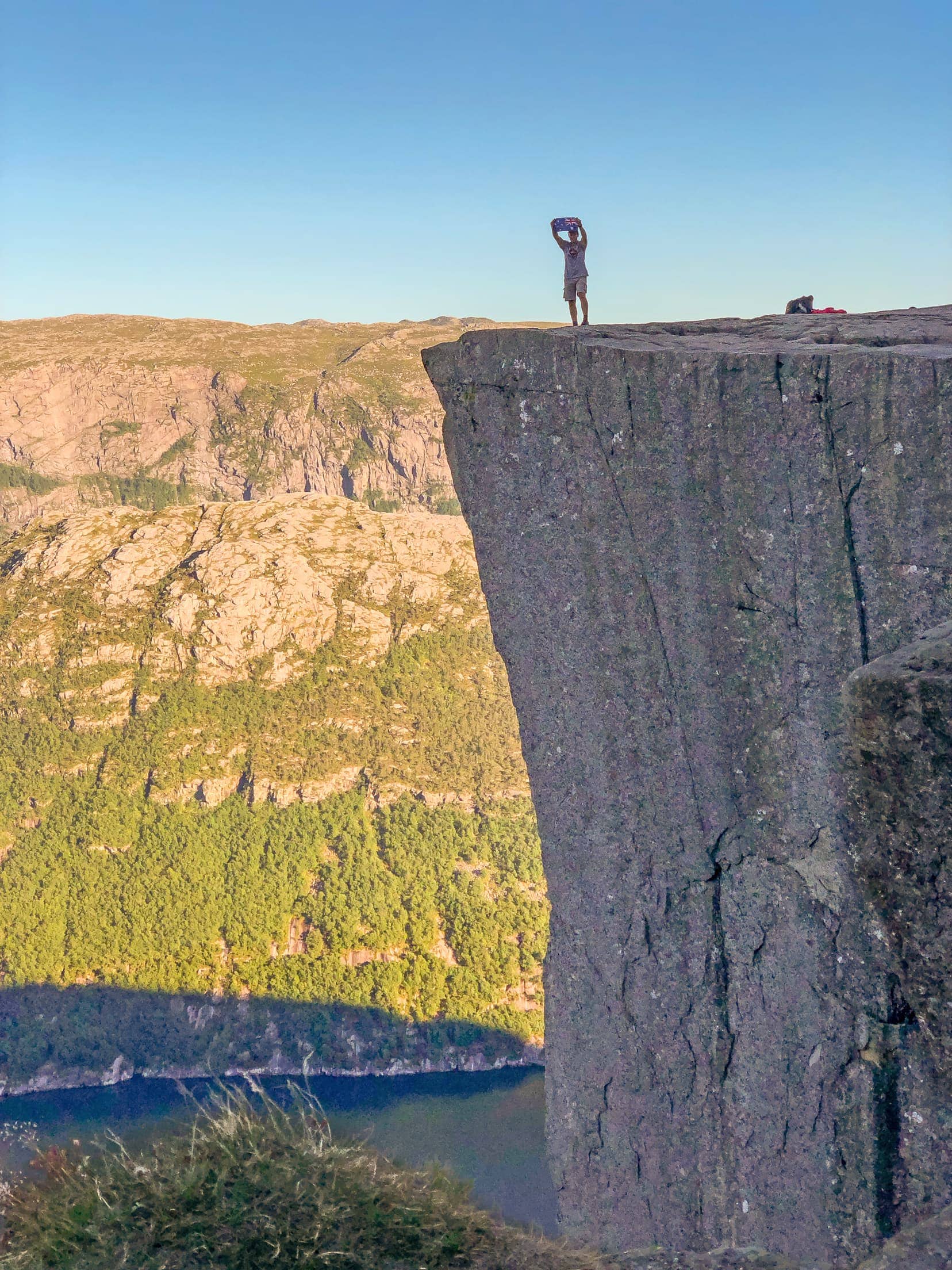 Man holding australian flag on a rock plateau with a fjord below