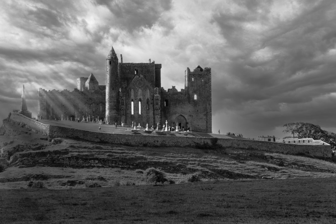 Church ruin on a hill with sun streaming through the dark clouds around it