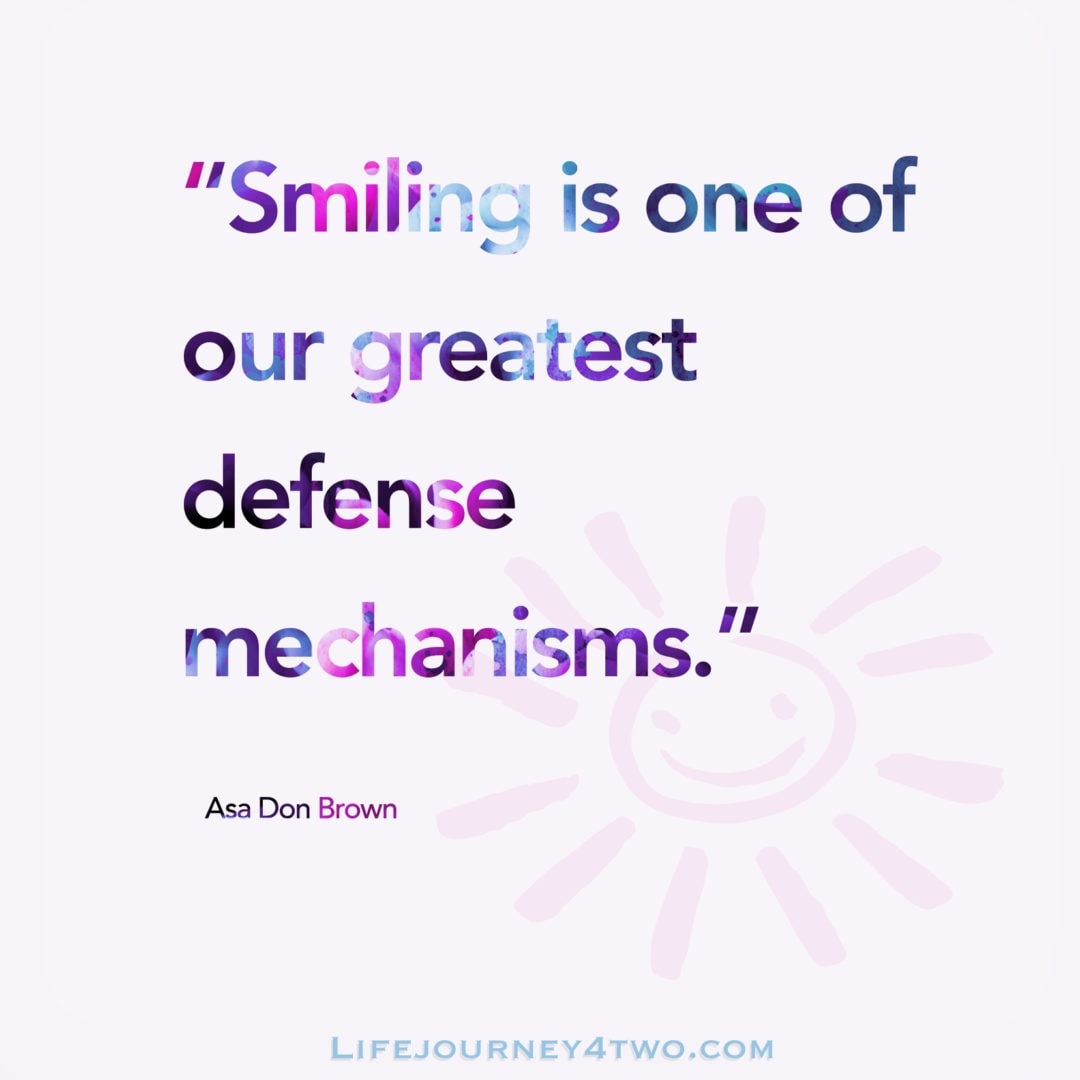 Smiling is one of our greatest defence mechanisms quote in blue and pink writing with a smiling sun