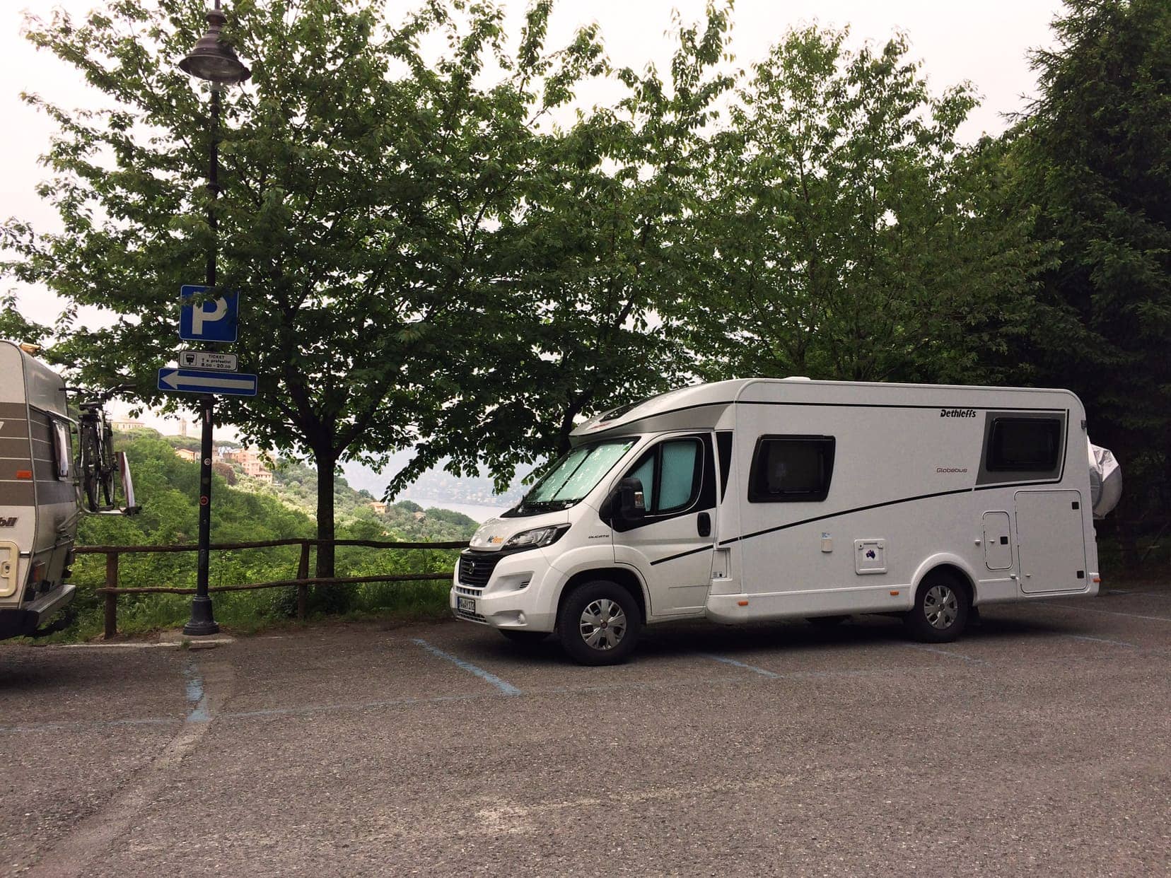 white motorhome parked by trees with ocean in background