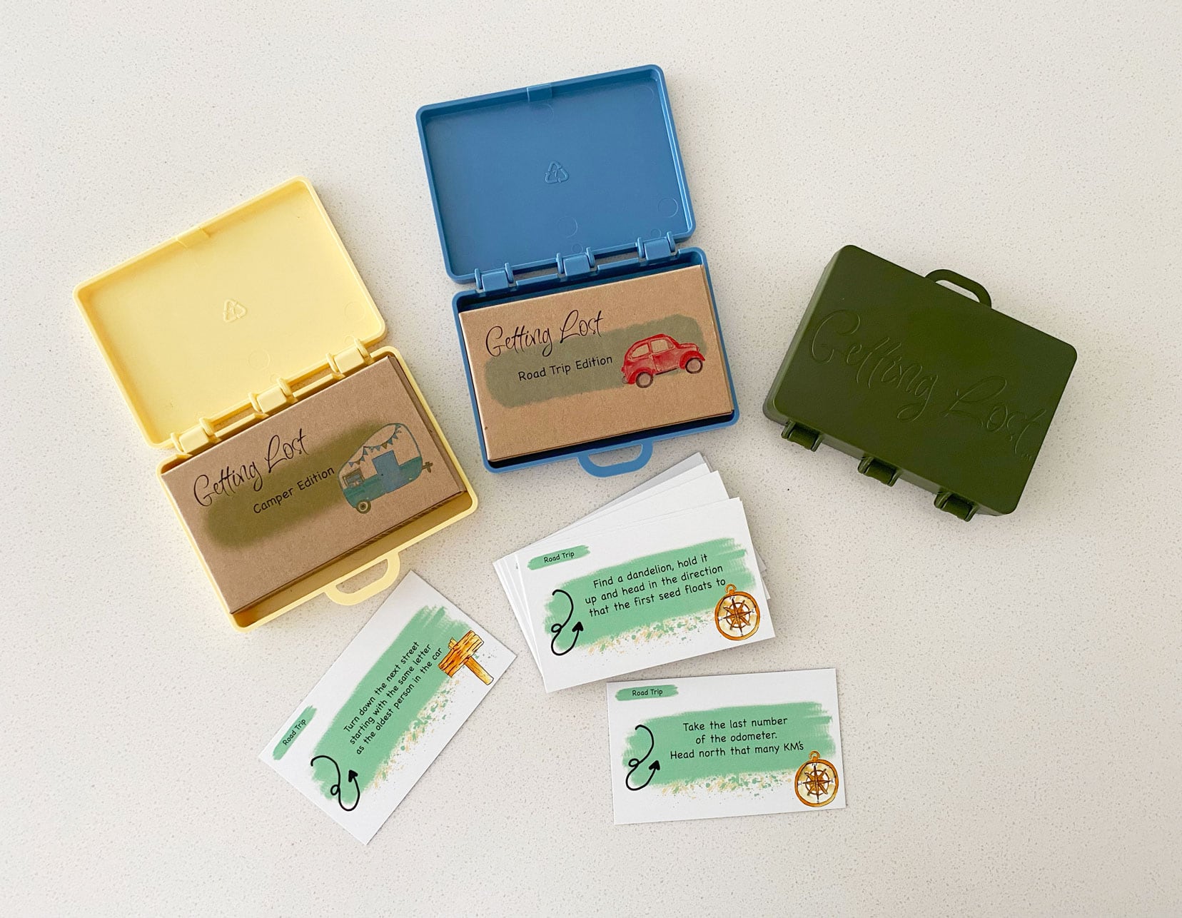 Three different versions of the game Getting Lost - road trip version, camper version and Australia version showing the cards and the little suitcase holders