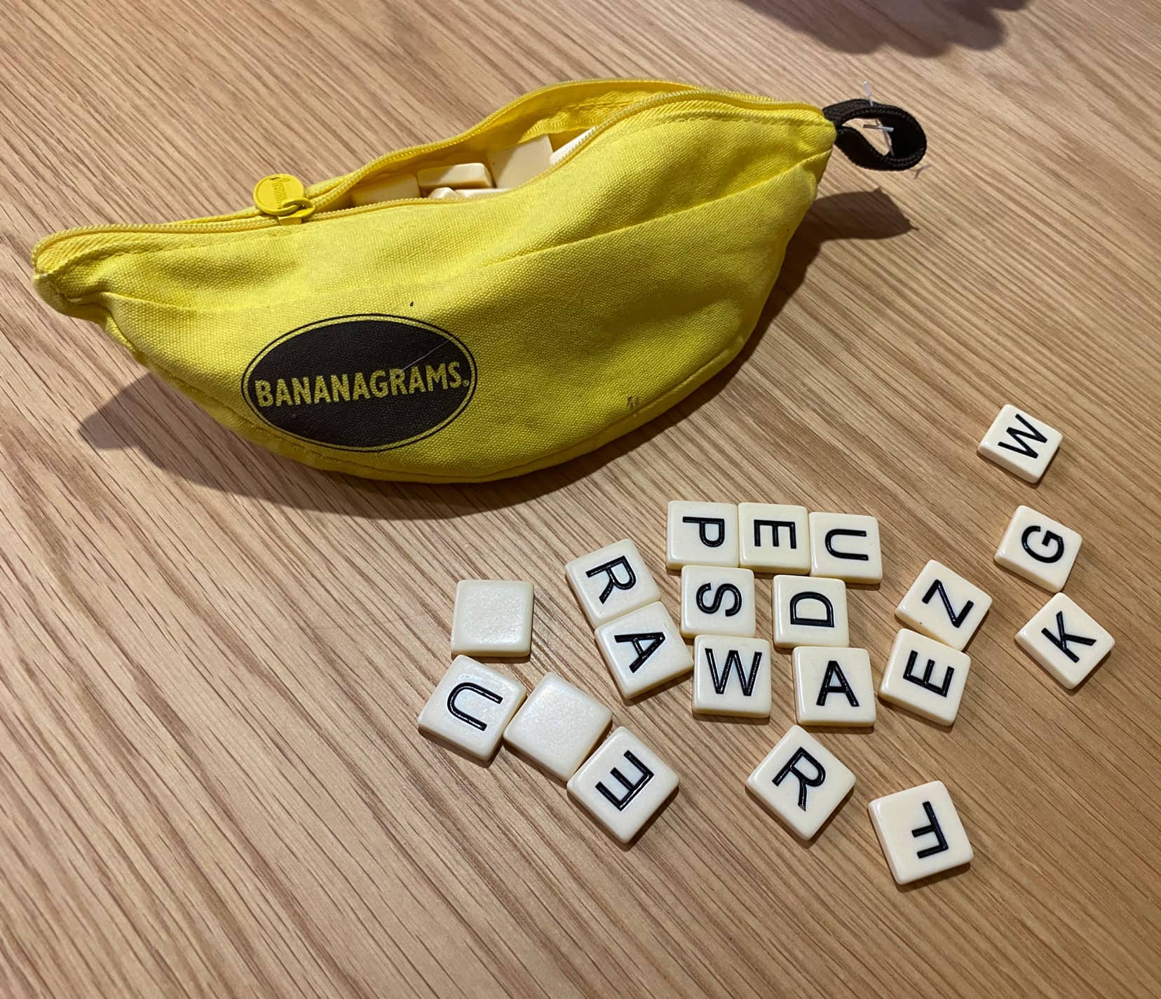 Bananagrams yellow banana shaped case with word tiles inside and a few scattered outside