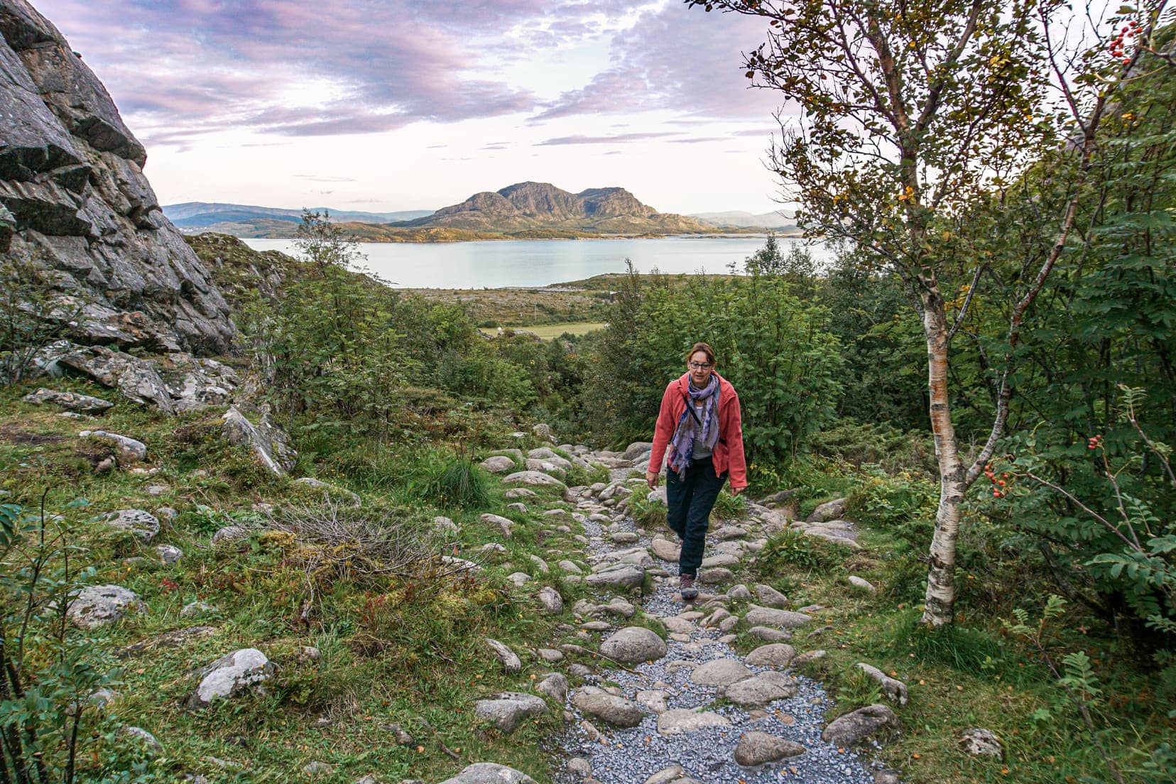 lady-walking-up-a-rocky-slope-with-a-mountain-and-sea-background