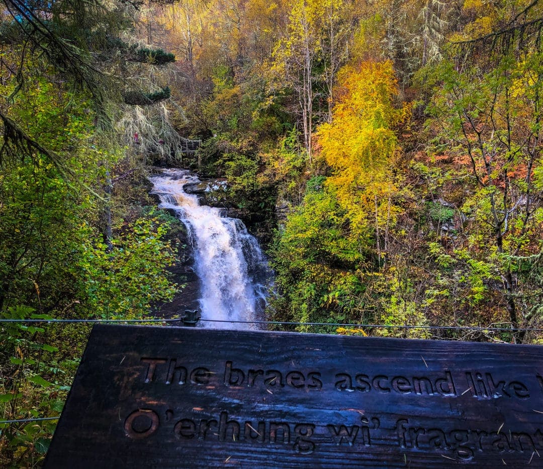 view of the Aberfeldy Falls with a wooden plank engraved with words of the Robert Burns poem