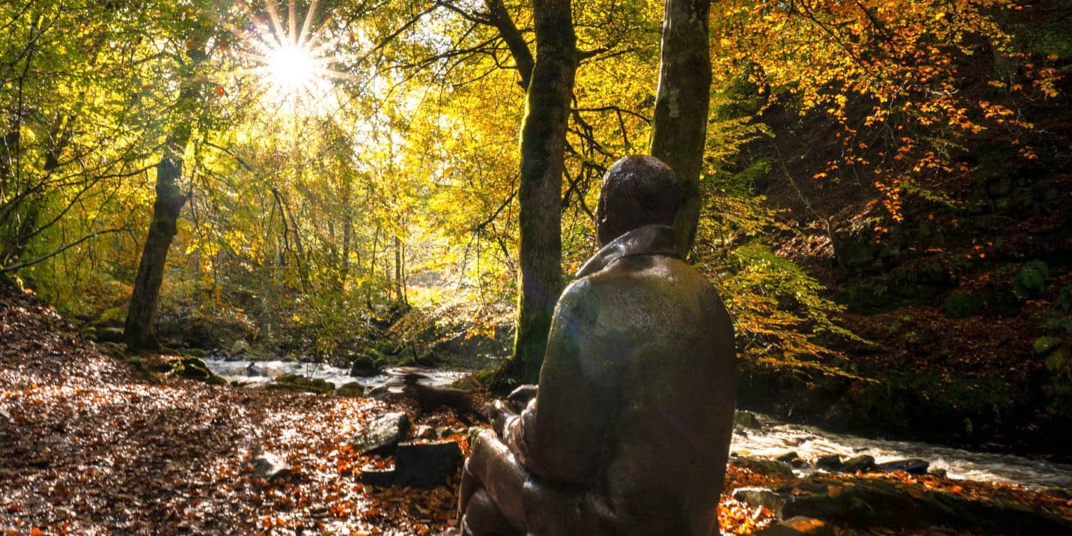 Birks of ABerfeldy Header photo of Robert Burns Statue with sun flare coming through the autumn trees