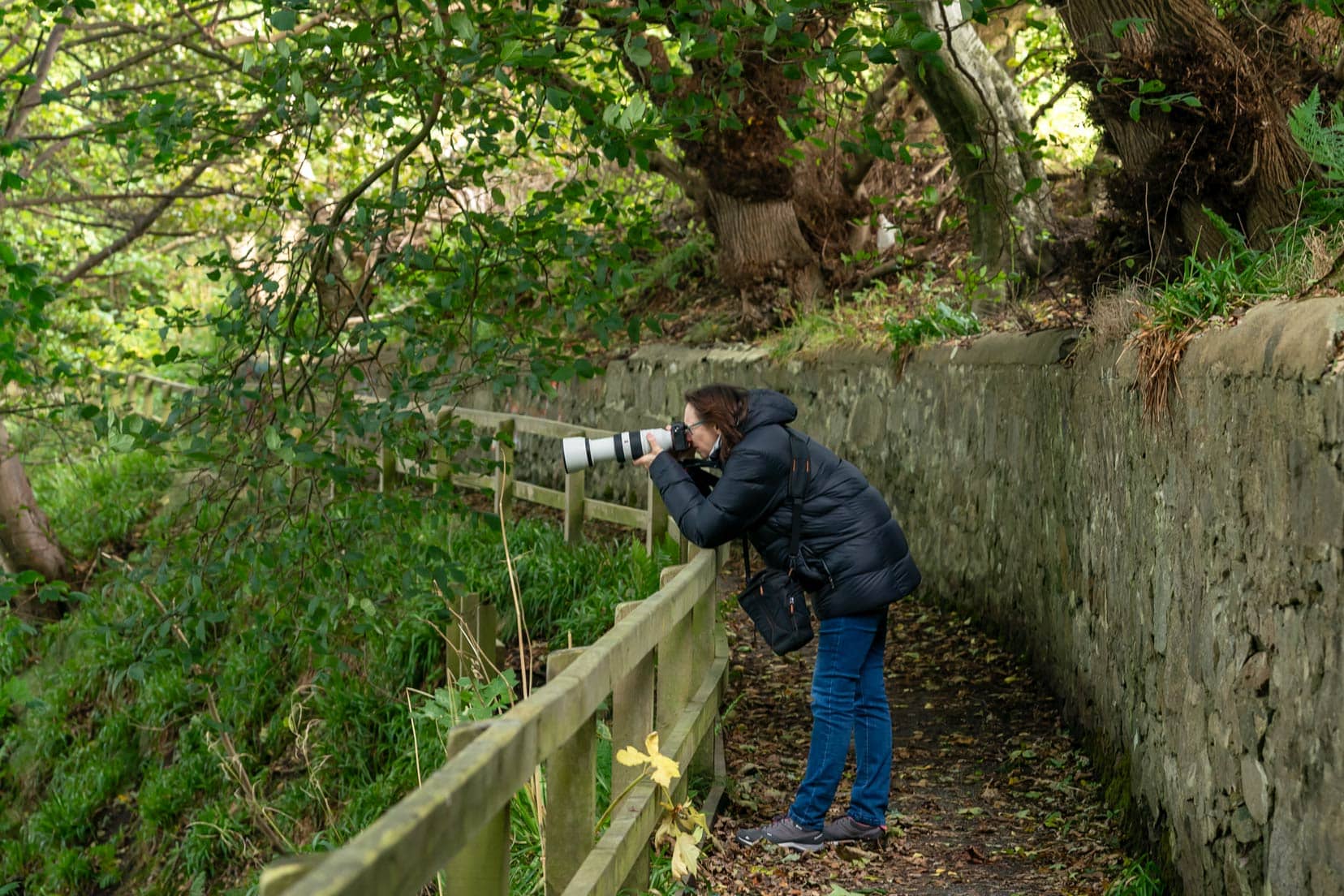 shelley shooting- with her camera from-the-southern-trail at Brig o balgownie with lots of leaves on the path and a stone wall behind her 