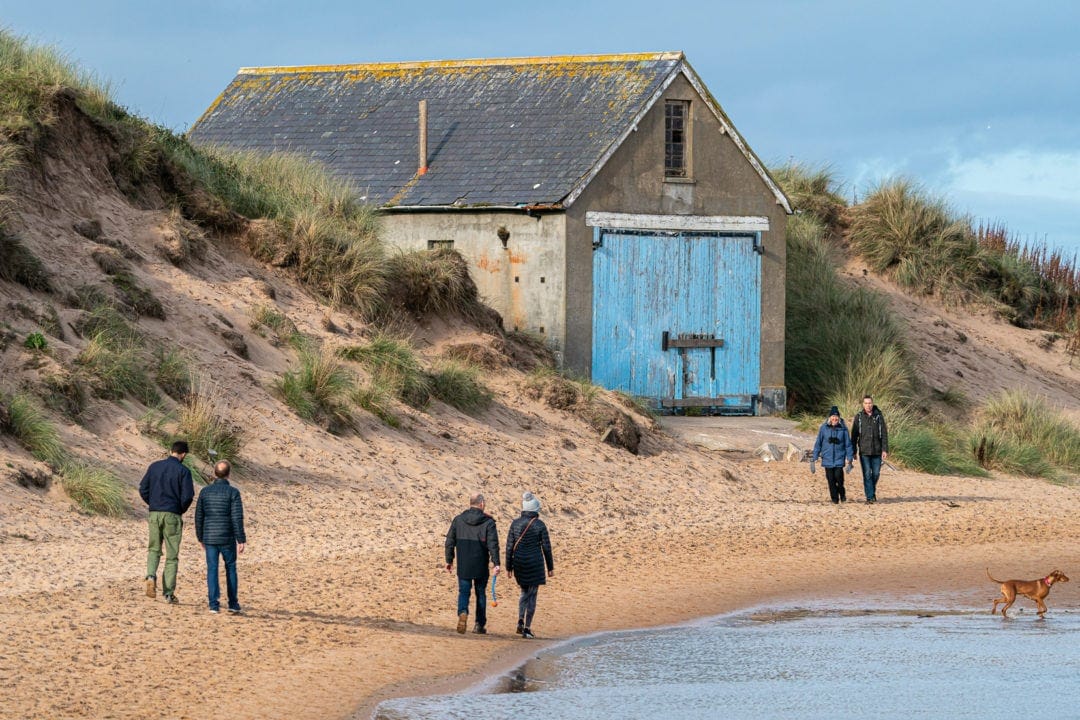 Newburgh Beach with people walking along and hut with blue doors 