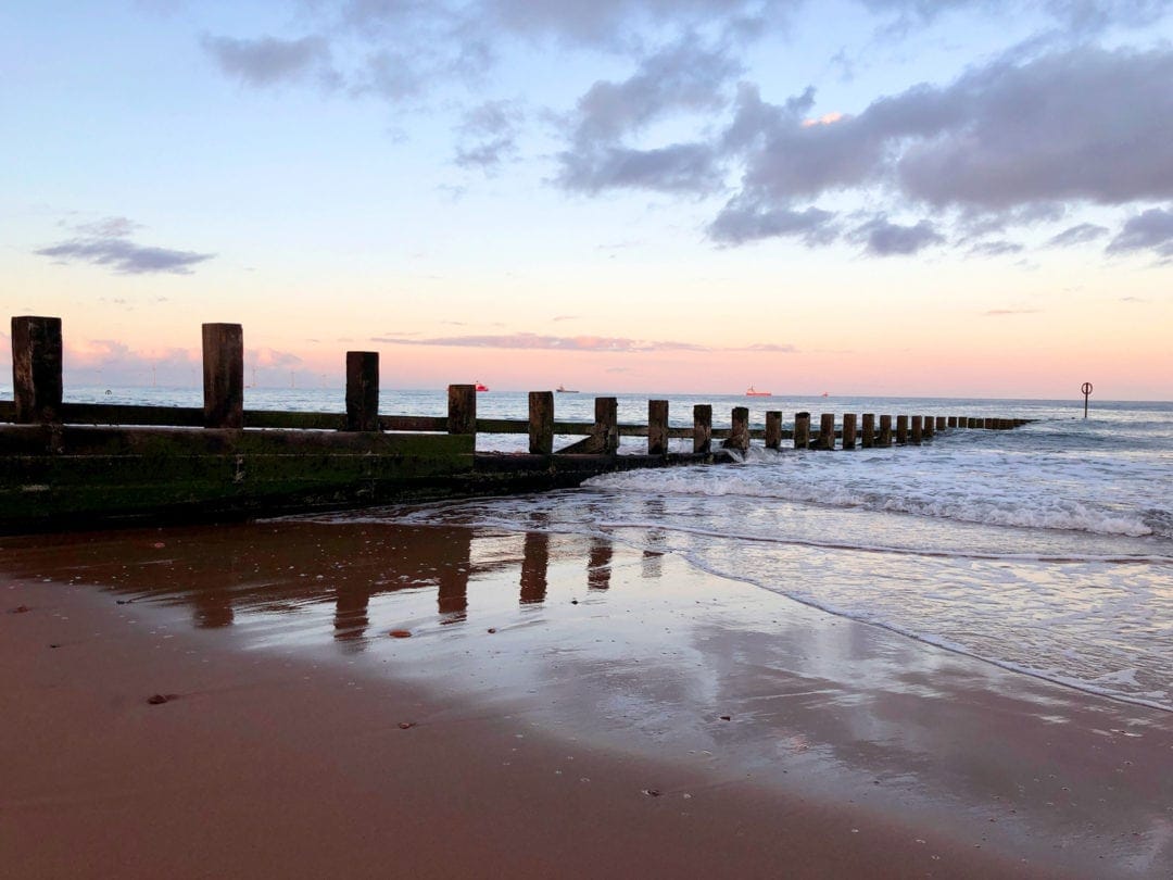 Aberdeen Beach at sunset with pinkish clouds and a pier stack going from the beach to the sea