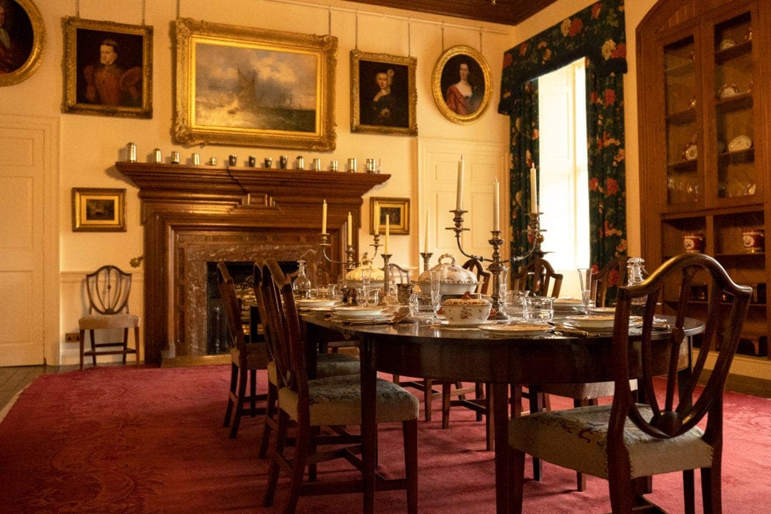 dining room with an oval wooden table set with fine dining ware and many portraits on the walls