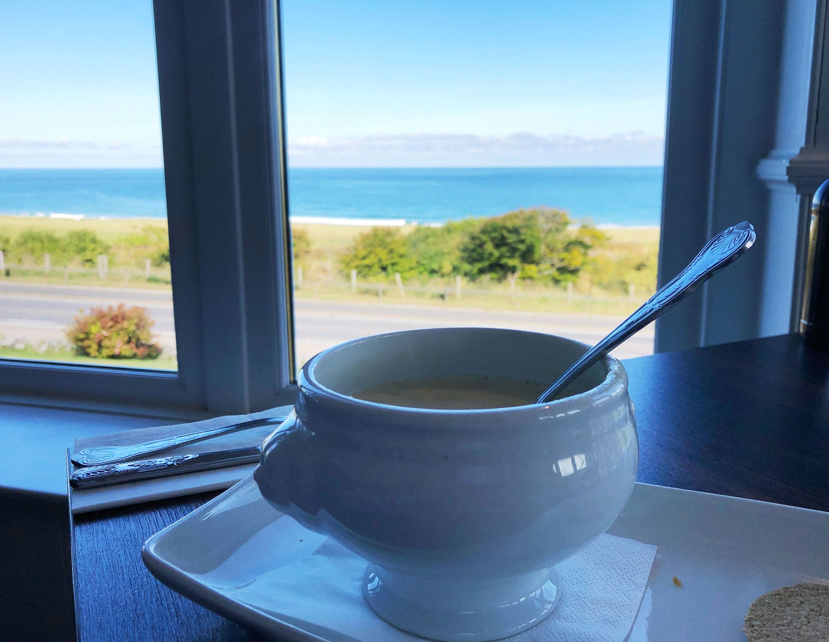 White soup bowl full of Cullen Skink with a back drop of a window with a sea view