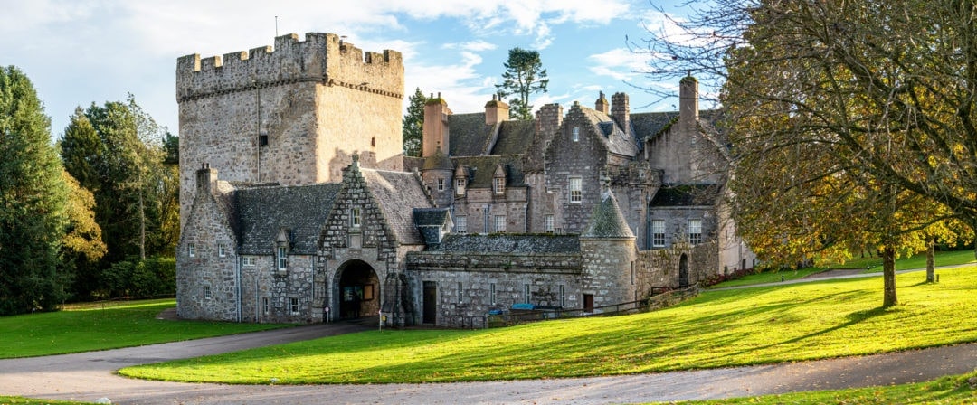 The front of Drum Castle showing the square tower, the mansion and green lawn 