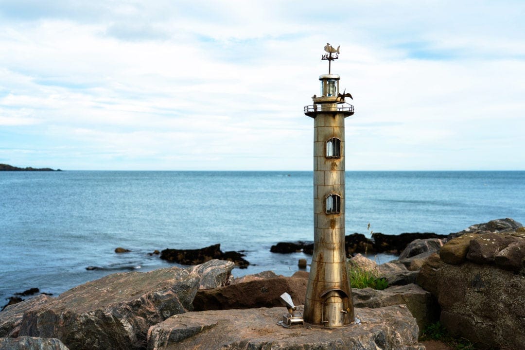 mini lighthouse sculpture attached to the rocks by the shore at Stonehaven