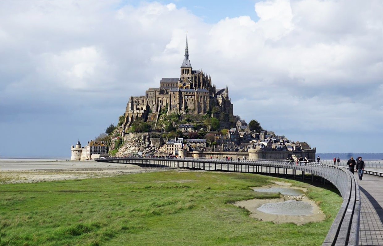 Mont-saint-michel in the background with a bridge leading to the island while tide is out. 