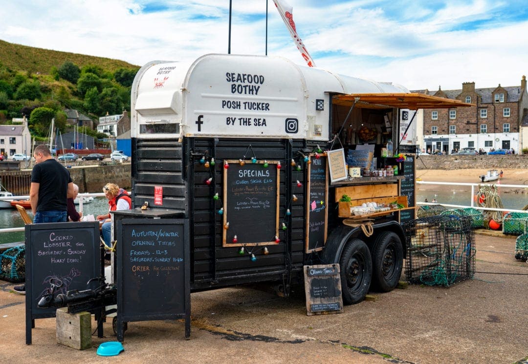 Stonehaven's seafood truck selling seafood, signs and truck with people eating behind the truck