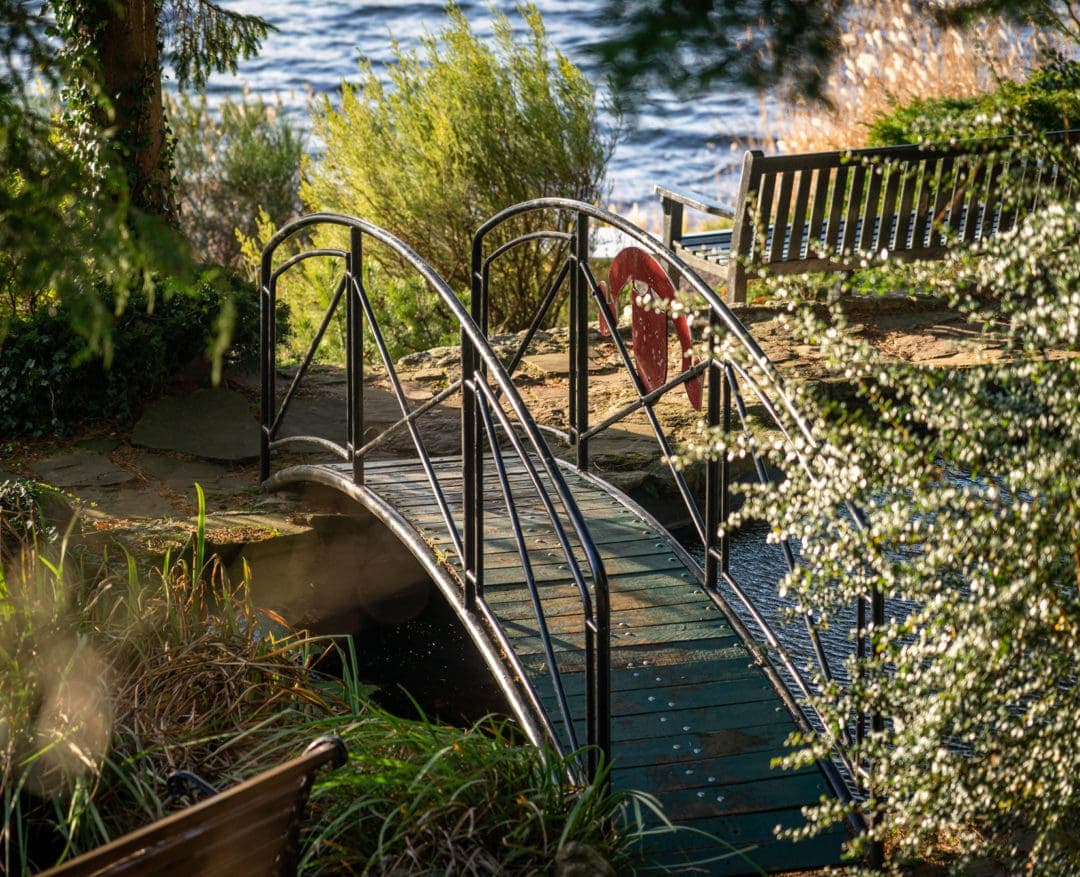 Small arched bridge over a small pond with teh loch in the back ground 