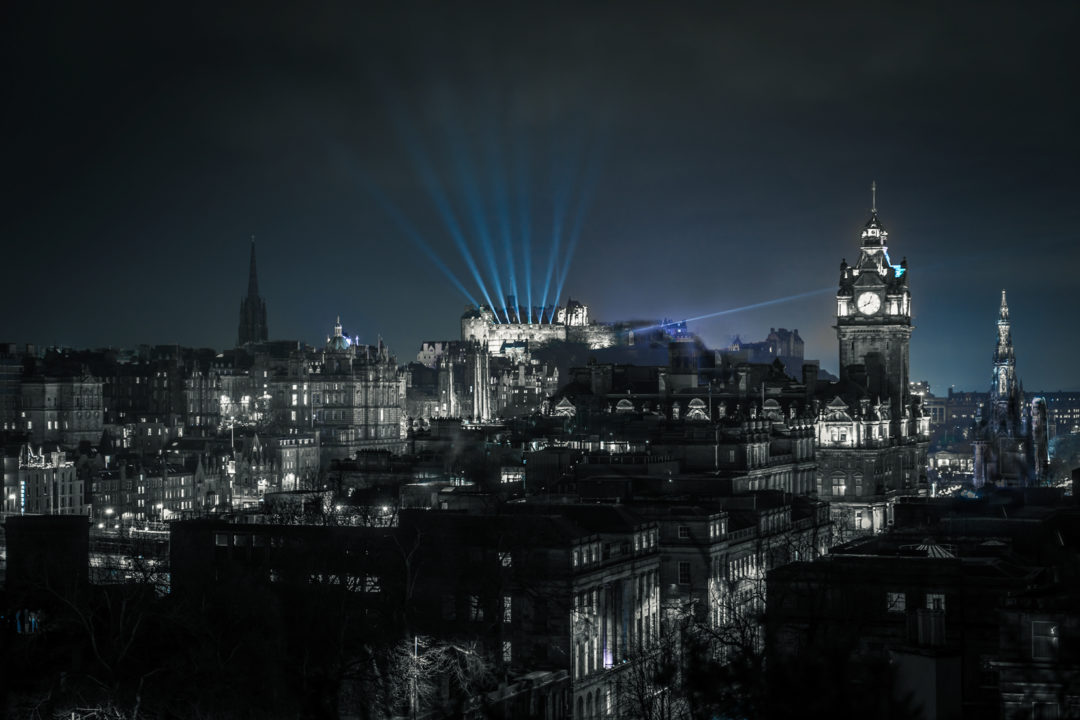  night scene of Edinburgh with blue laser beams coming from the top of Edinburgh castle