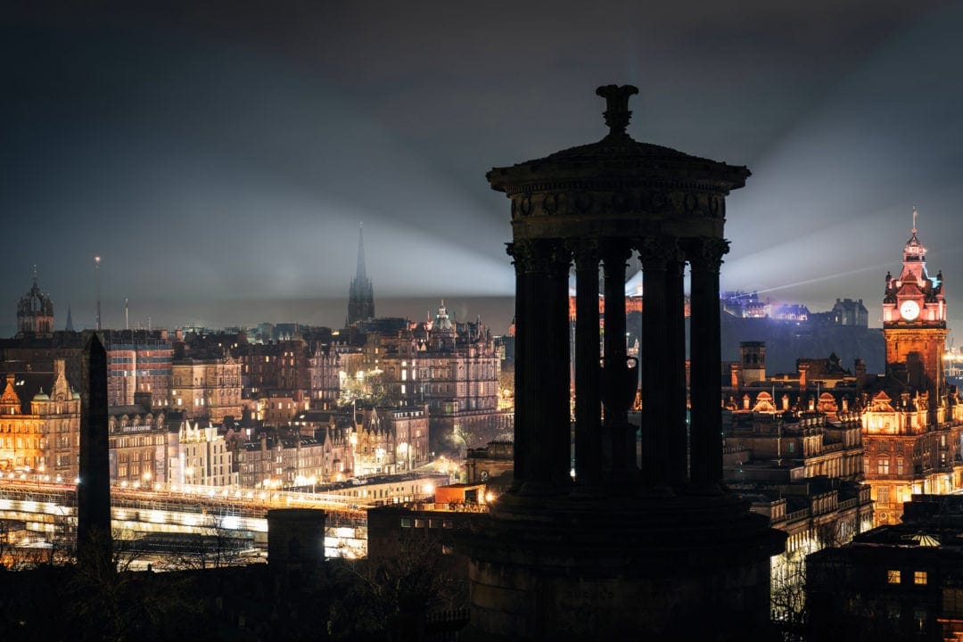 Edinburgh night scape with Dugald Stewart monument in foreground and lights of Edinburgh castle across the city