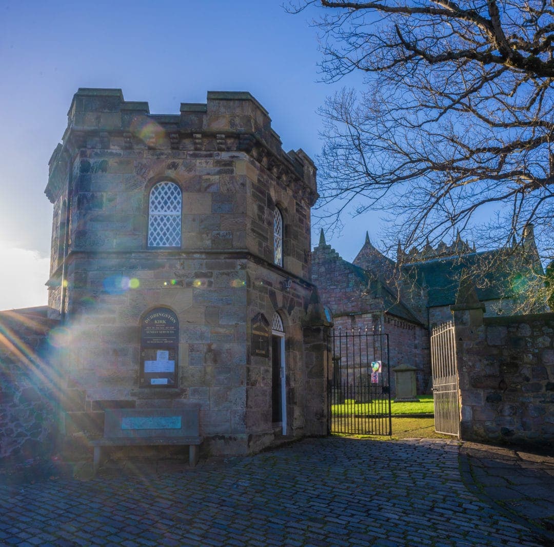 Duddingston Kirk Gatehouse with sun streaming in to the side of the shot and a view throught the gate to the graveyard