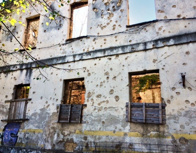 Wall of derelict house full of bullet holes and pock marks from mortar bombs