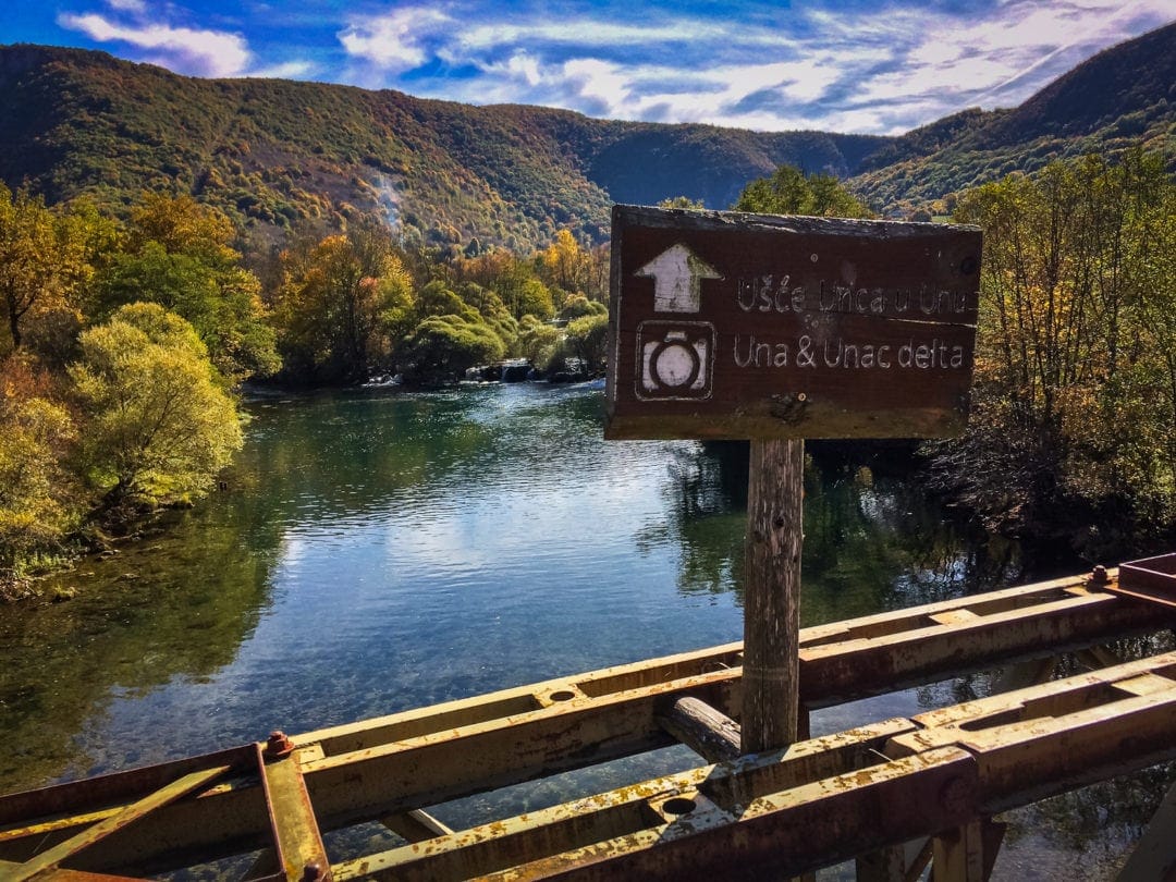 Brown sign on a bridge pointing towards River Una 