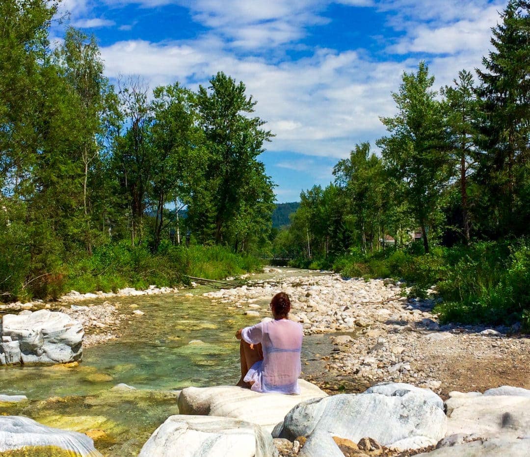 Ferlach-Campsite-by-river with woman sitting on rock lookiing at stream and trees