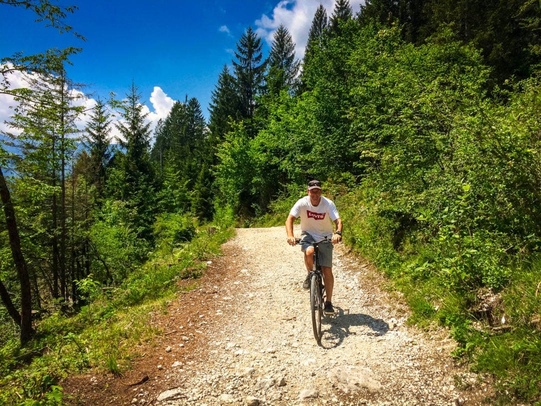 Lars cycling around Lake Bohinj on a gravelly path with pine trees  lining the path