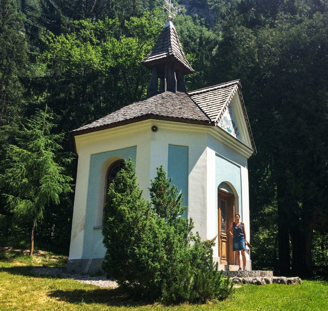 Tiny chapel with pale blue walls and pine trees behind 