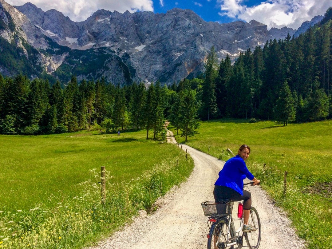 Cycling on a path with meadows either side and Mountains-in-Jezersko in the background