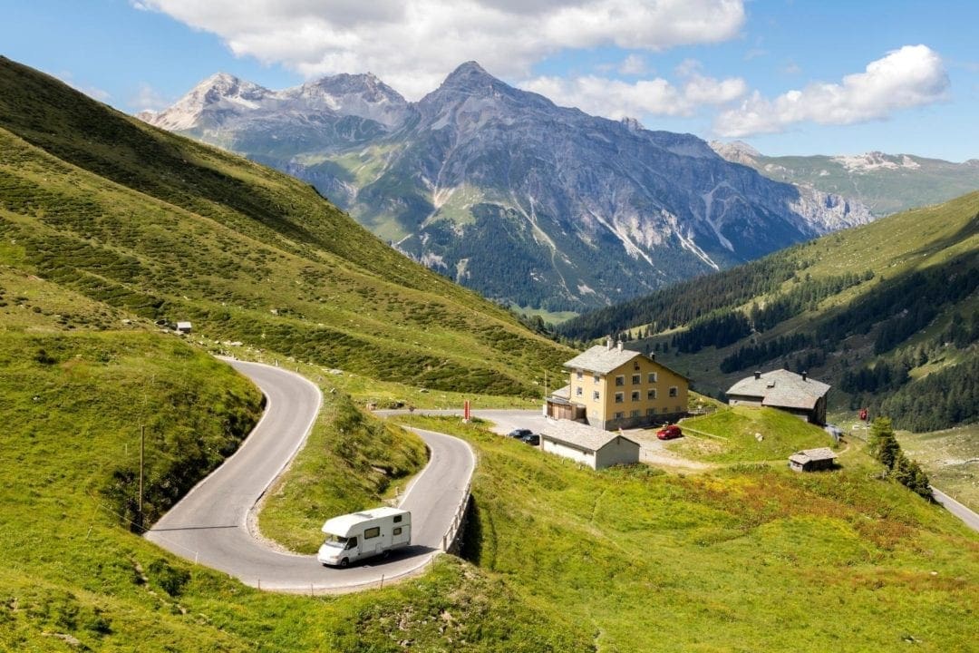 winding road with a motorhome on it with mountains in the background