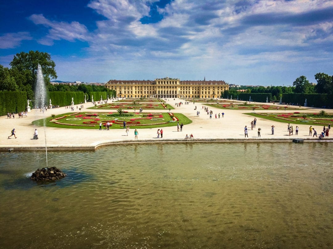 Schonbrunn- Palace with paths and  formal flower beds in front of the palace. A lake with a fountain are in the foreground