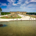 Schonbrunn- Palace with paths and formal flower beds in front of the palace. A lake with a fountain are in the foreground