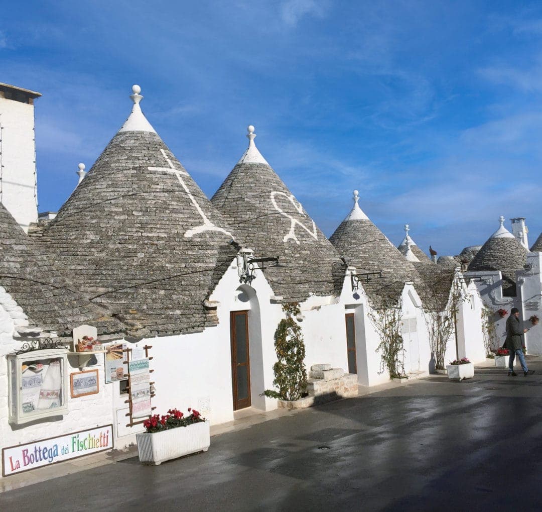 Alberobello trulli on a street with the white symbols painted on the conical roofs. 