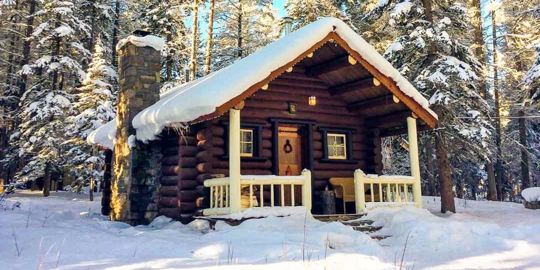 log cabin in forest covered in snow