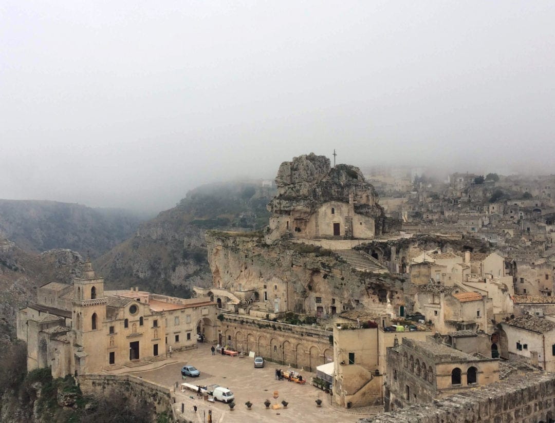 Matera cream buildings with a church on a high central part with fog seeping through the image
