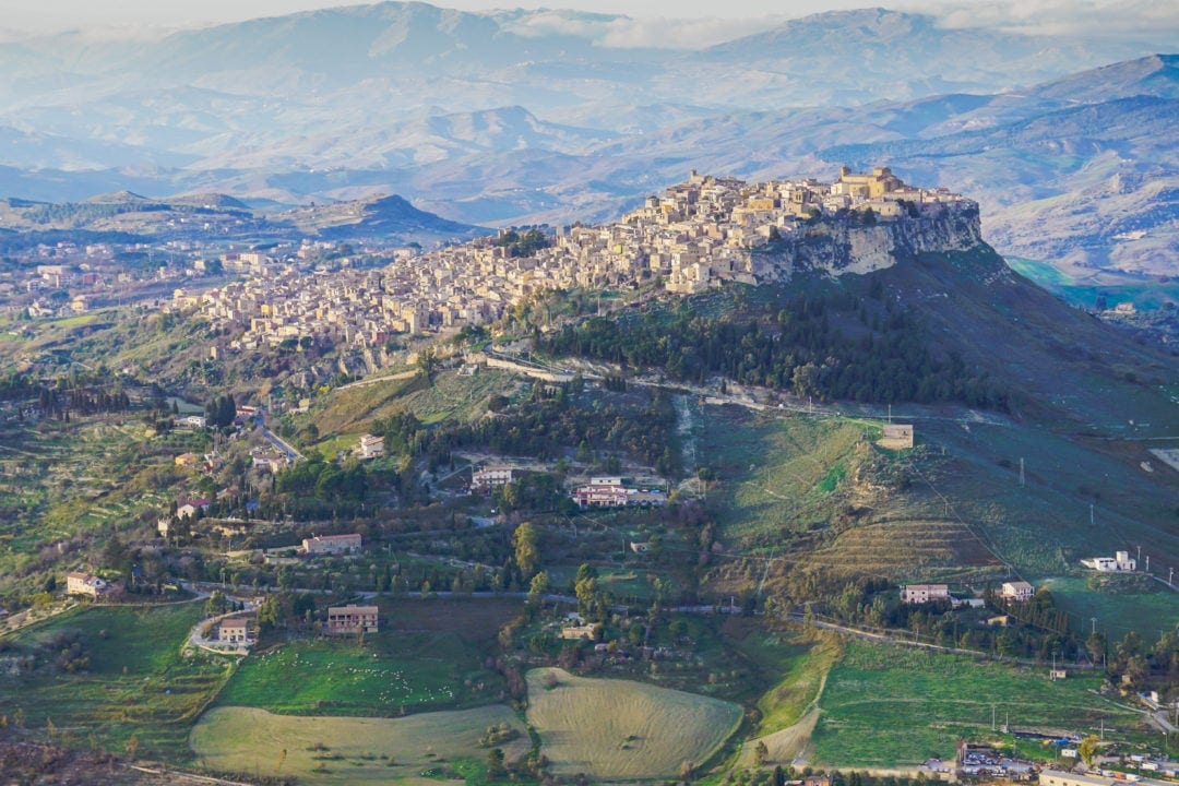 view of white and beige houses on a hill top surrounded by green plateaus