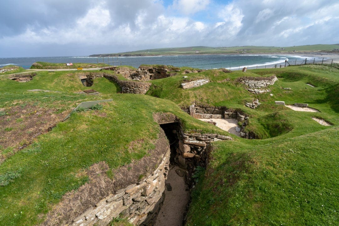 View of Skara Brae grass mo9und with dug out rooms and ocean in the background
