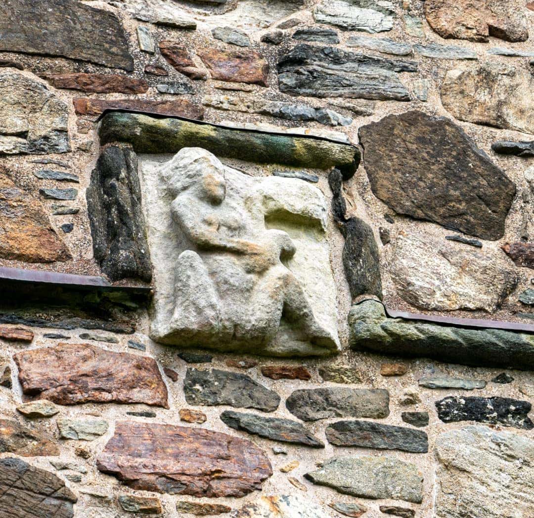 A small stone sculpture on the chuch wall of a woman with legs open