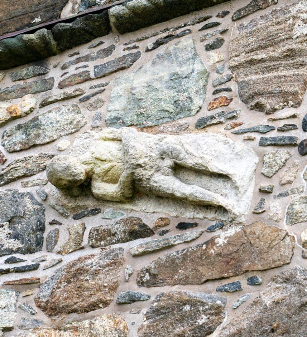 a sculpture on the chucch wall of a man holding his private partsl 
