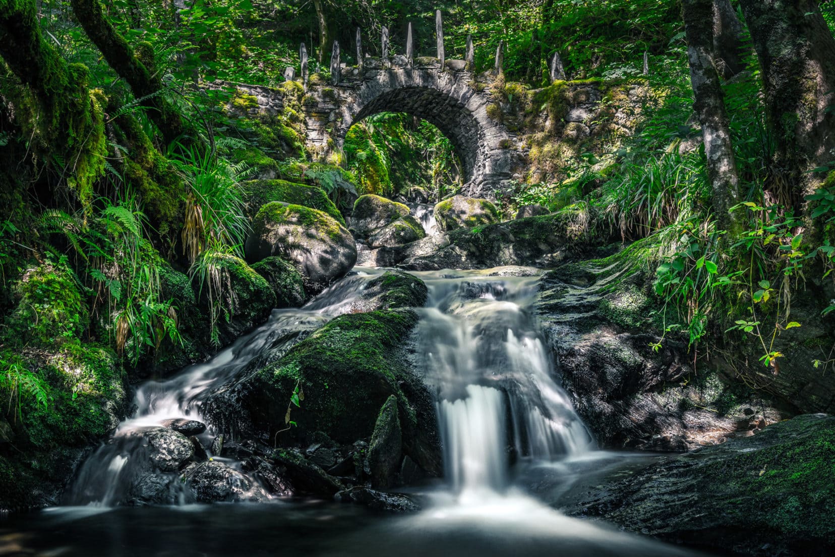long exposure shot of stream with curved stone bridge in background