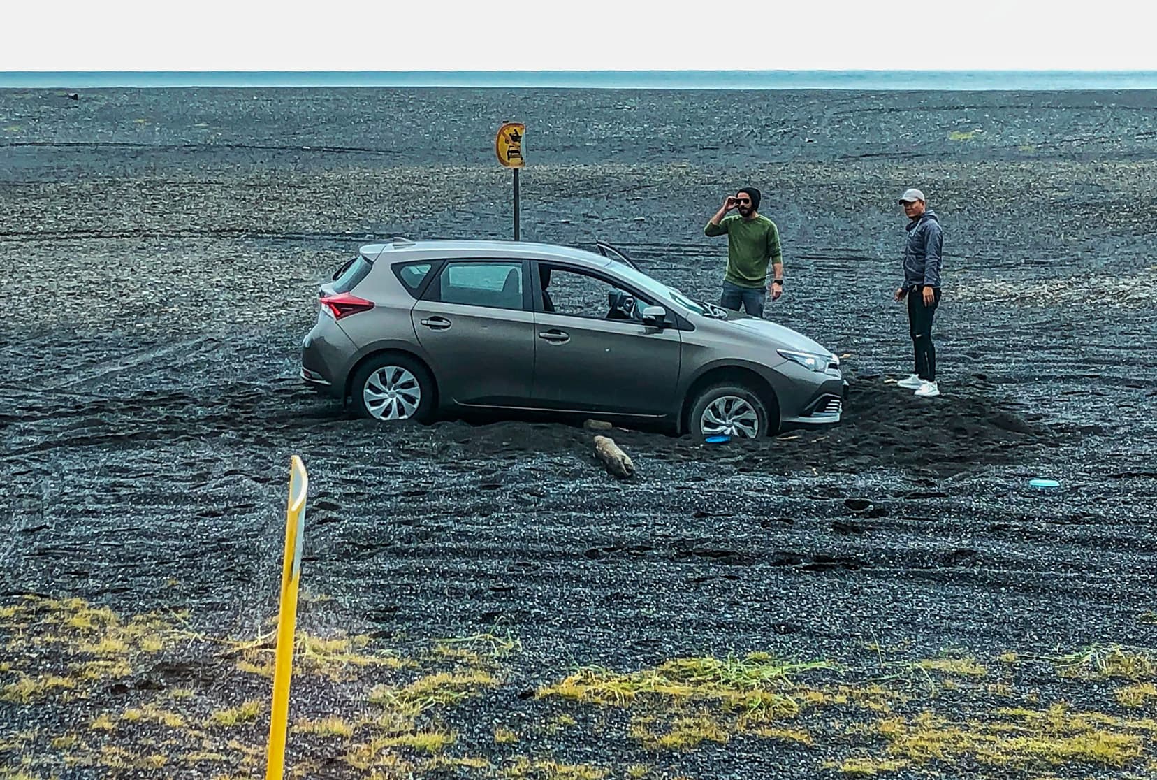 car bogged in black sand with guy on phone