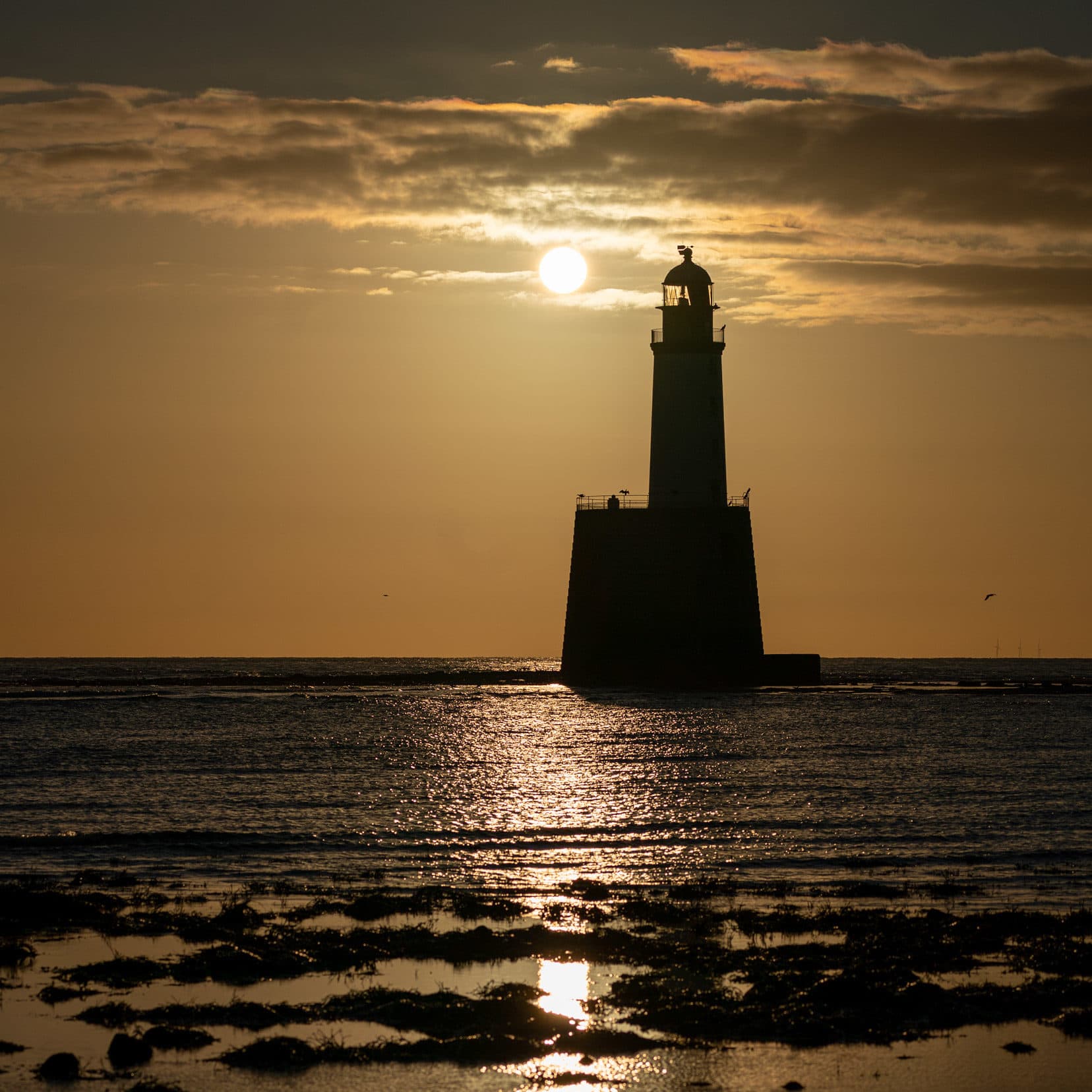 lighthouse seen at sunrise from the shore