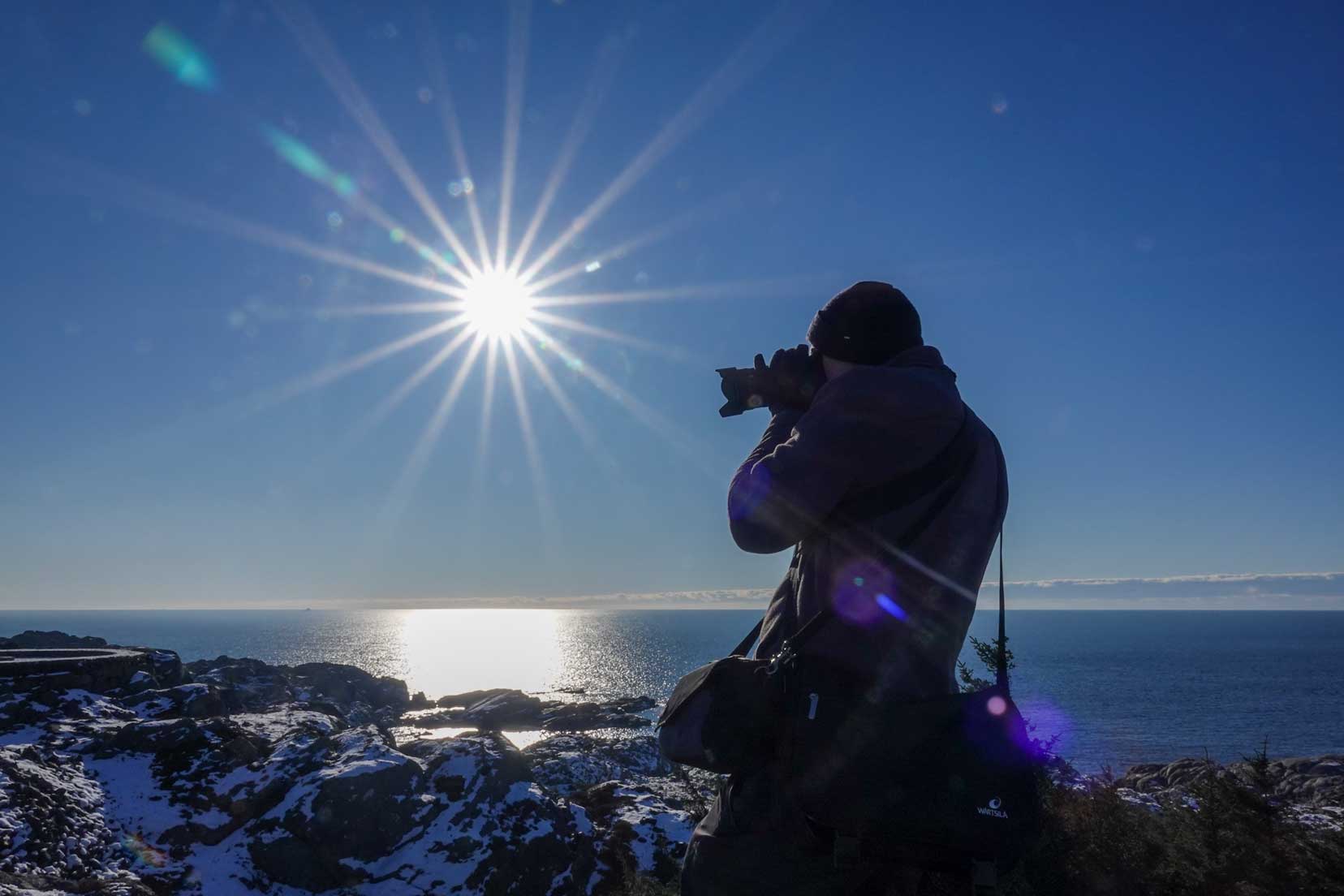 Sun-star-in-Norway with man taking photo in foreground and ocean in teh background